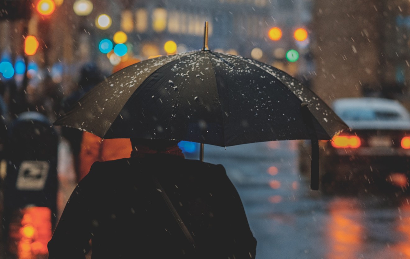 Person with umbrella in the snow at night, looking down a busy street